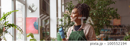 Attractive smiling florist stands near windows on background of her own floral decor studio 100552194