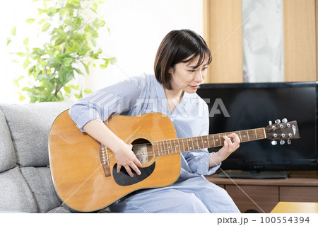 ソファーに座ってギターを弾いて微笑む女性 100554394