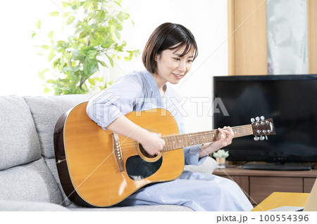 ソファーに座ってギターを弾いて微笑む女性 ソファーに座ってギターを弾いて微笑む女性 100554396