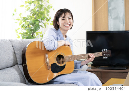 ソファーに座ってギターを弾いて微笑む女性 100554404