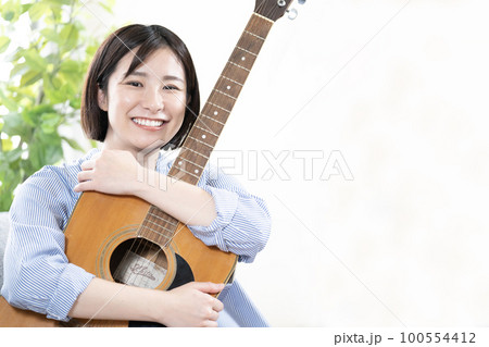 ソファーに座ってギターを抱いて微笑む女性 100554412