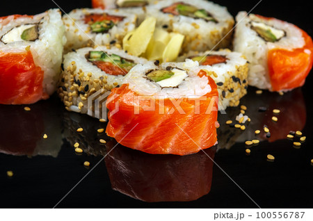 Traditional sushi with sesame seeds - Philadelphia with salmon, avocado and cheese. Japanese cuisine on black background Traditional sushi with sesame seeds - Philadelphia with salmon, avocado and cheese. Japanese cuisine on black background 100556787