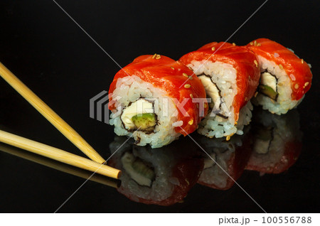 Traditional sushi and chopsticks - Philadelphia with salmon, avocado and cheese. Japanese cuisine on black background Traditional sushi and chopsticks - Philadelphia with salmon, avocado and cheese. Japanese cuisine on black background 100556788