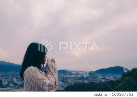 朝日を浴び街をバックに佇むコーヒーカップを持った女性の写真 100567552