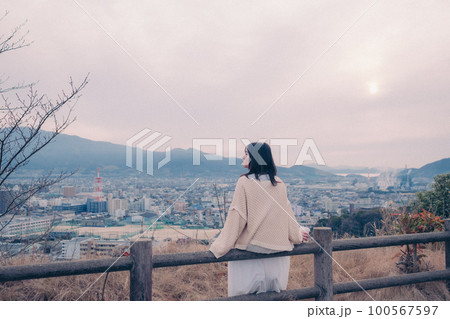 朝日を浴び街をバックに佇むコーヒーカップを持った女性の写真 100567597