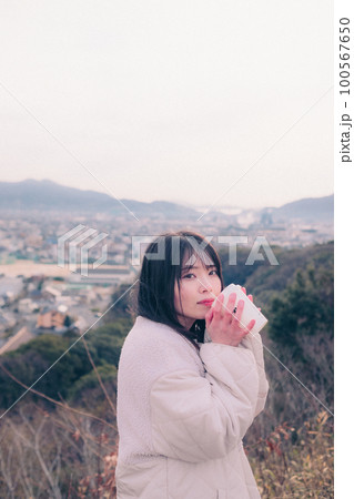 朝日を浴び街をバックに佇むコーヒーカップを持った女性の写真 100567650