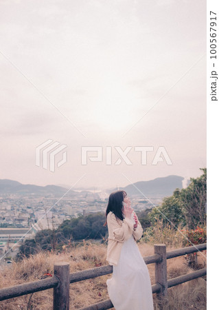 朝日を浴び街をバックに佇むスマホを持った女性の写真 100567917