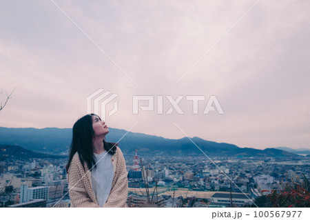 朝日を浴び街をバックに佇む女性の写真 100567977