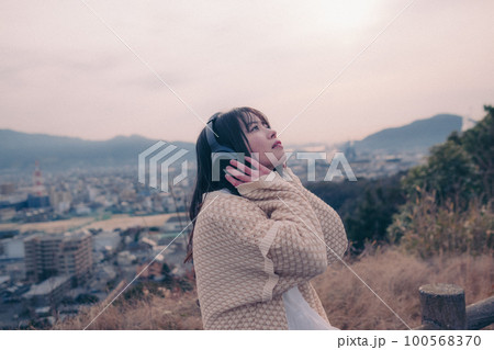 朝日を浴び街をバックに音楽を聴く女性の写真 朝日を浴び街をバックに音楽を聴く女性の写真 100568370