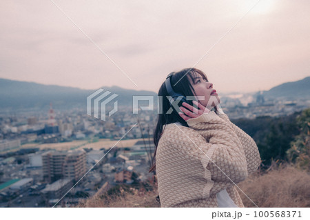 朝日を浴び街をバックに音楽を聴く女性の写真 朝日を浴び街をバックに音楽を聴く女性の写真 100568371