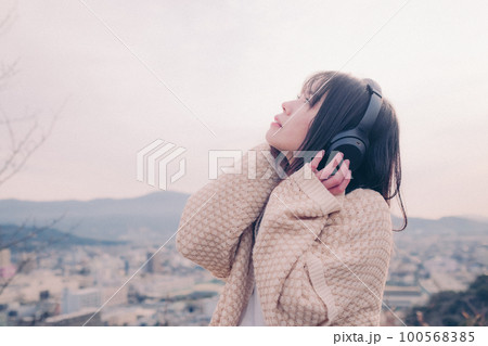 朝日を浴び街をバックに音楽を聴く女性の写真 朝日を浴び街をバックに音楽を聴く女性の写真 100568385
