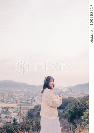 朝日を浴び街をバックに音楽を聴く女性の写真 100568517