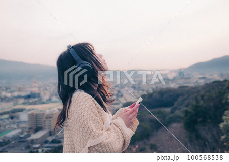 朝日を浴び街をバックに音楽を聴く女性の写真 朝日を浴び街をバックに音楽を聴く女性の写真 100568538