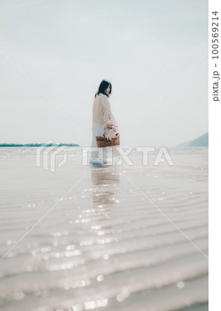 海辺にドライフラワーとカゴを持って佇む女性の写真 100569214