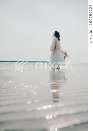 海辺にドライフラワーとカゴを持って佇む女性の写真 100569222