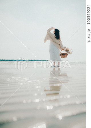海辺にドライフラワーとカゴを持って佇む女性の写真 100569224
