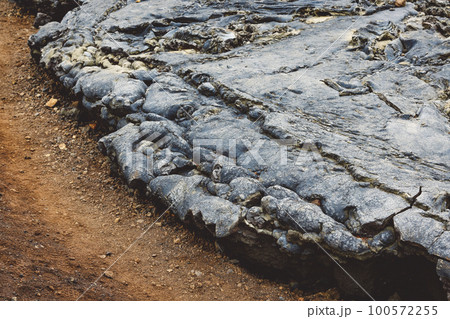 Cooled lava touching the dirt where it stopped running, forming a curved edge of black volcanic rock Cooled lava touching the dirt where it stopped running, forming a curved edge of black volcanic rock 100572255