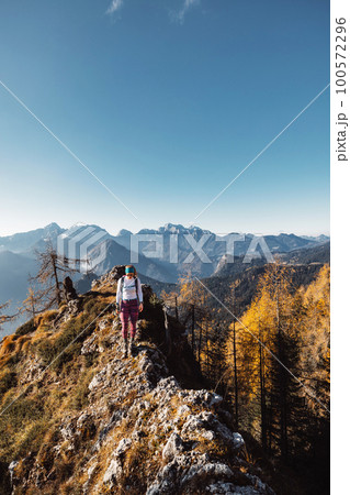 Vertical photo of female mountaineer hiking on the mountain ridge with the background of autumn mountains  100572296