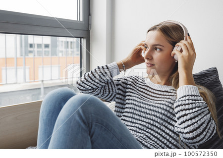 Young caucasian woman looking out the window from her bed while listening to some music Young caucasian woman looking out the window from her bed while listening to some music 100572350