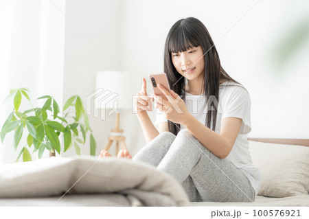 朝ベッドに座ってスマホを見る女子高生 朝ベッドに座ってスマホを見る女子高生 100576921