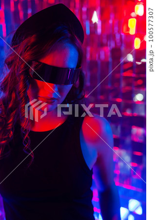 Close-up portrait of a caucasian woman in sunglasses in neon light against a mirror wall.  100577307