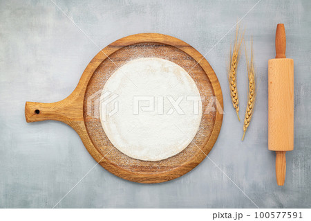 Homemade pizza dough in wooden pizza platter with wheat ears set up on grey concrete background flat lay and copy space 100577591