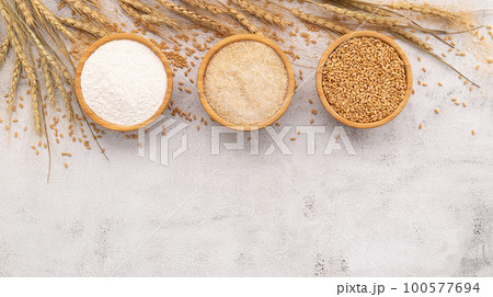 Wheat grains , brown wheat flour and white wheat flour in wooden bowl set up on white concrete background. 100577694