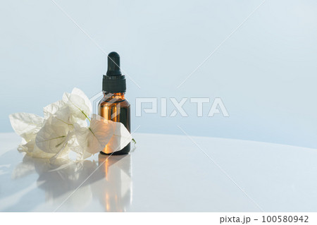 Natural medicine or essential aroma oil or beauty essence amber glass vial with dropper with white flowers and airy blue background. Face and body spa serum care concept banner 100580942