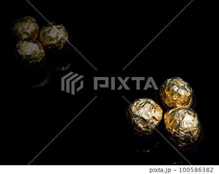 Round candies in golden foil on a black background. 100586382
