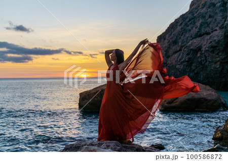 Woman in a red flying dress on the ocean or on the sea beach against the backdrop of the sunset sky. Woman in a red flying dress on the ocean or on the sea beach against the backdrop of the sunset sky. 100586872