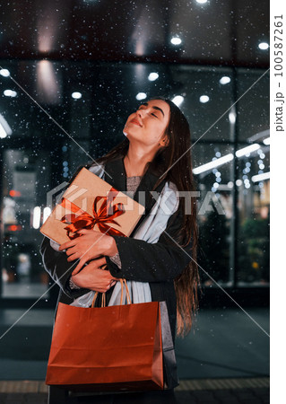 From the shop with gift box in hands. Cheerful woman is outdoors at Christmas holidays time. Conception of new year From the shop with gift box in hands. Cheerful woman is outdoors at Christmas holidays time. Conception of new year 100587261