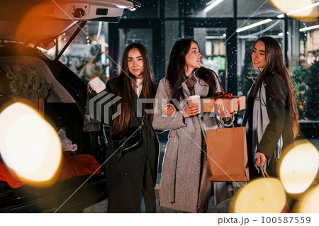 Cups of drink in hands. Three cheerful women spends Christmas holidays together outdoors. Conception of new year 100587559