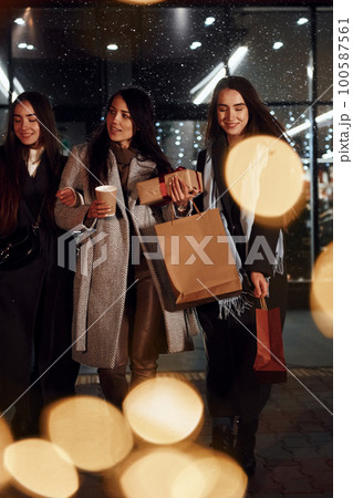 Cups of drink in hands. Three cheerful women spends Christmas holidays together outdoors. Conception of new year 100587561