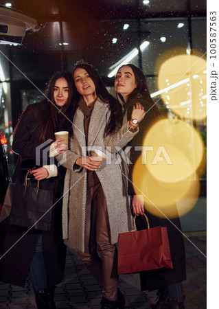 Cups of drink in hands. Three cheerful women spends Christmas holidays together outdoors. Conception of new year 100587563