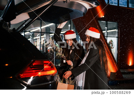 Standing near car's back trunk opened. Happy sisters twins spends Christmas holidays together outdoors. Conception of new year 100588269