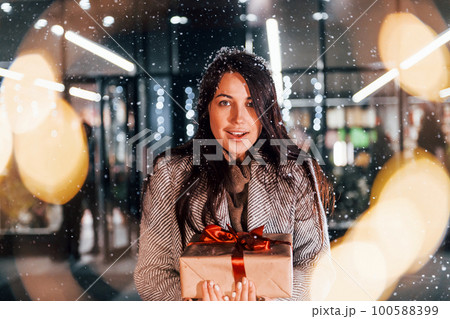 Holds gift box in hands. Cheerful woman is outdoors at Christmas holidays time. Conception of new year Holds gift box in hands. Cheerful woman is outdoors at Christmas holidays time. Conception of new year 100588399