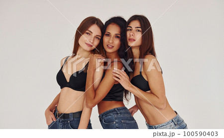 Three young women in lingerie together indoors. White background 100590403