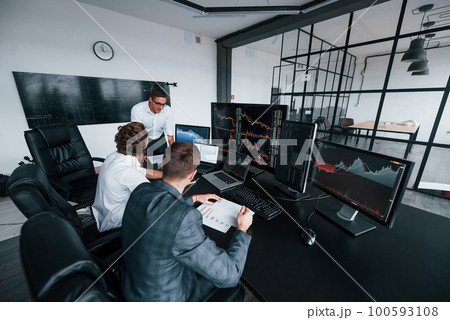 Holds document in hands. Team of stockbrokers works in modern office with many display screens Holds document in hands. Team of stockbrokers works in modern office with many display screens 100593108