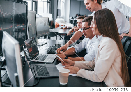Analysing information. Team of stockbrokers works in modern office with many display screens 100594258