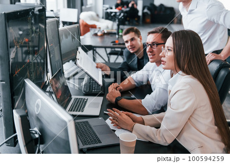 Analysing information. Team of stockbrokers works in modern office with many display screens 100594259