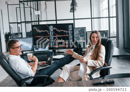 Woman and man have conversation. Team of stockbrokers works in modern office with many display screens Woman and man have conversation. Team of stockbrokers works in modern office with many display screens 100594721