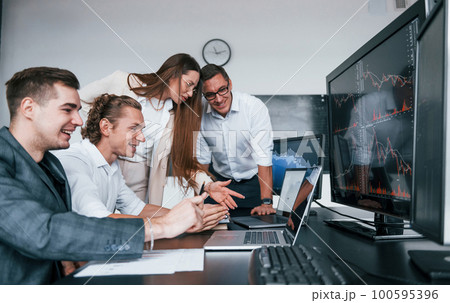 Tracks the graphs. Team of stockbrokers works in modern office with many display screens 100595396
