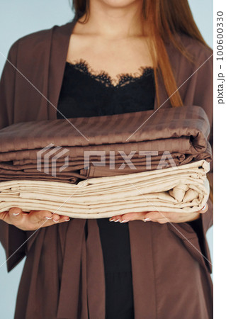 Close up view of young woman that standing against wall with bed clothes in hands Close up view of young woman that standing against wall with bed clothes in hands 100600330
