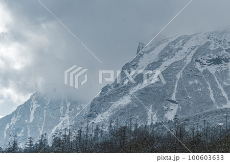 Winter Cloudy Foggy Mountain Landscape. Snow-covered mountain covered with floating rainy clouds. 100603633