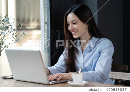 Young asian woman look at her laptop smiling near the window with coffee 100613037