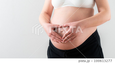 Hands folded in the shape of a heart on the middle of the belly of a pregnant girl 100613277