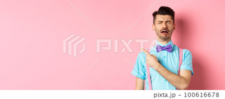 Sad and lonely man in bow-tie crying and pointing finger left, feeling miserable and complaining, sulking while standing on pink background Sad and lonely man in bow-tie crying and pointing finger left, feeling miserable and complaining, sulking while standing on pink background 100616678