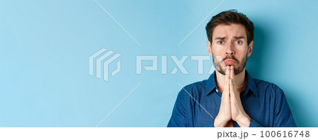 Sad young man begging for help, apoligizing and sobbing miserable, standing on blue background Sad young man begging for help, apoligizing and sobbing miserable, standing on blue background 100616748