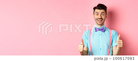 Excited caucasian guy showing thumbs up and praising great work, well done gesture, standing in suspenders and bow-tie on pink background Excited caucasian guy showing thumbs up and praising great work, well done gesture, standing in suspenders and bow-tie on pink background 100617083