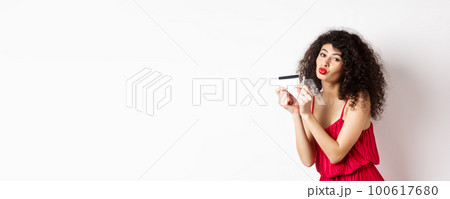 Shopping. Beautiful lady with curly hair, pucker lips, kissing plastic credit card, standing in red dress against white background Shopping. Beautiful lady with curly hair, pucker lips, kissing plastic credit card, standing in red dress against white background 100617680